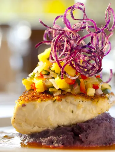 Seared fish fillet topped with tropical fruit salsa, garnished with spiraled vegetables, served on purple mashed potatoes