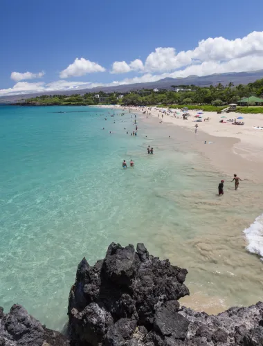 Wide view of Hapuna Beach with turquoise waters, white sand, and visitors enjoying the shoreline on a sunny day.