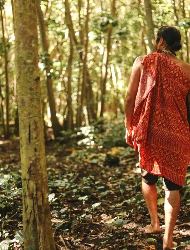 A man in cultural garb walks through a forest on the island of Molokai
