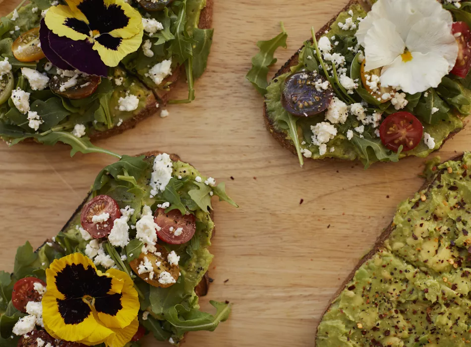 Avocado toast topped with arugula, cherry tomatoes, crumbled feta, and edible flowers.